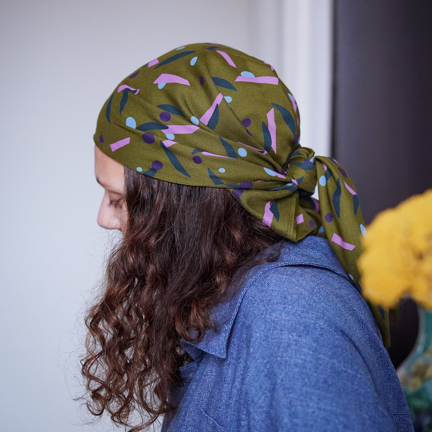 Foulard triangulaire vert kaki coloré noué dans des cheveux longs chatains bouclés